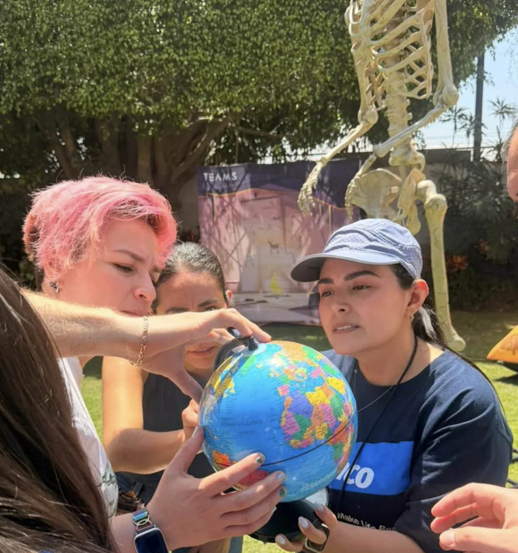 Equipo analiza pistas en globo terráqueo al aire libre con lona de TEAMS al fondo durante la experiencia Indiana Jones en Guadalajara